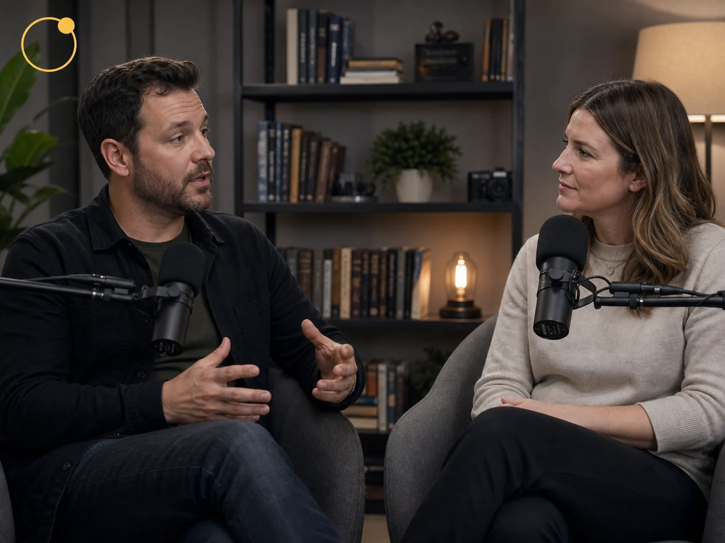 Two people talking at a podcast table with a small ring logo in the upper left.